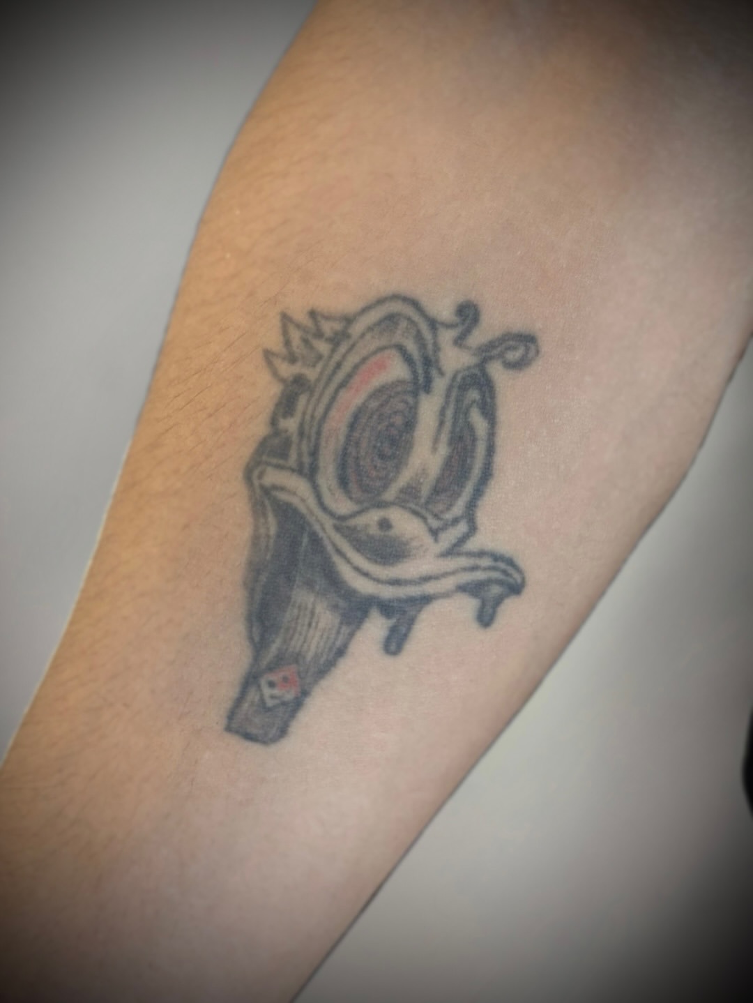 Faded cartoon character tattoo on forearm before cover-up.