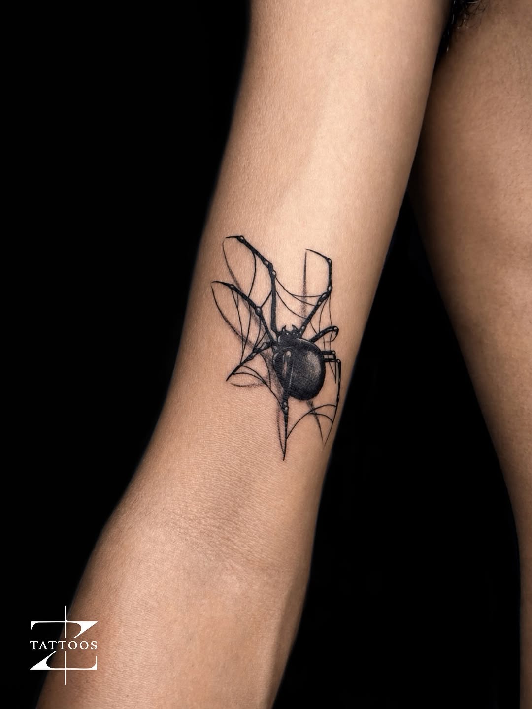Black-and-grey realism spider on a web wrapping the forearm.