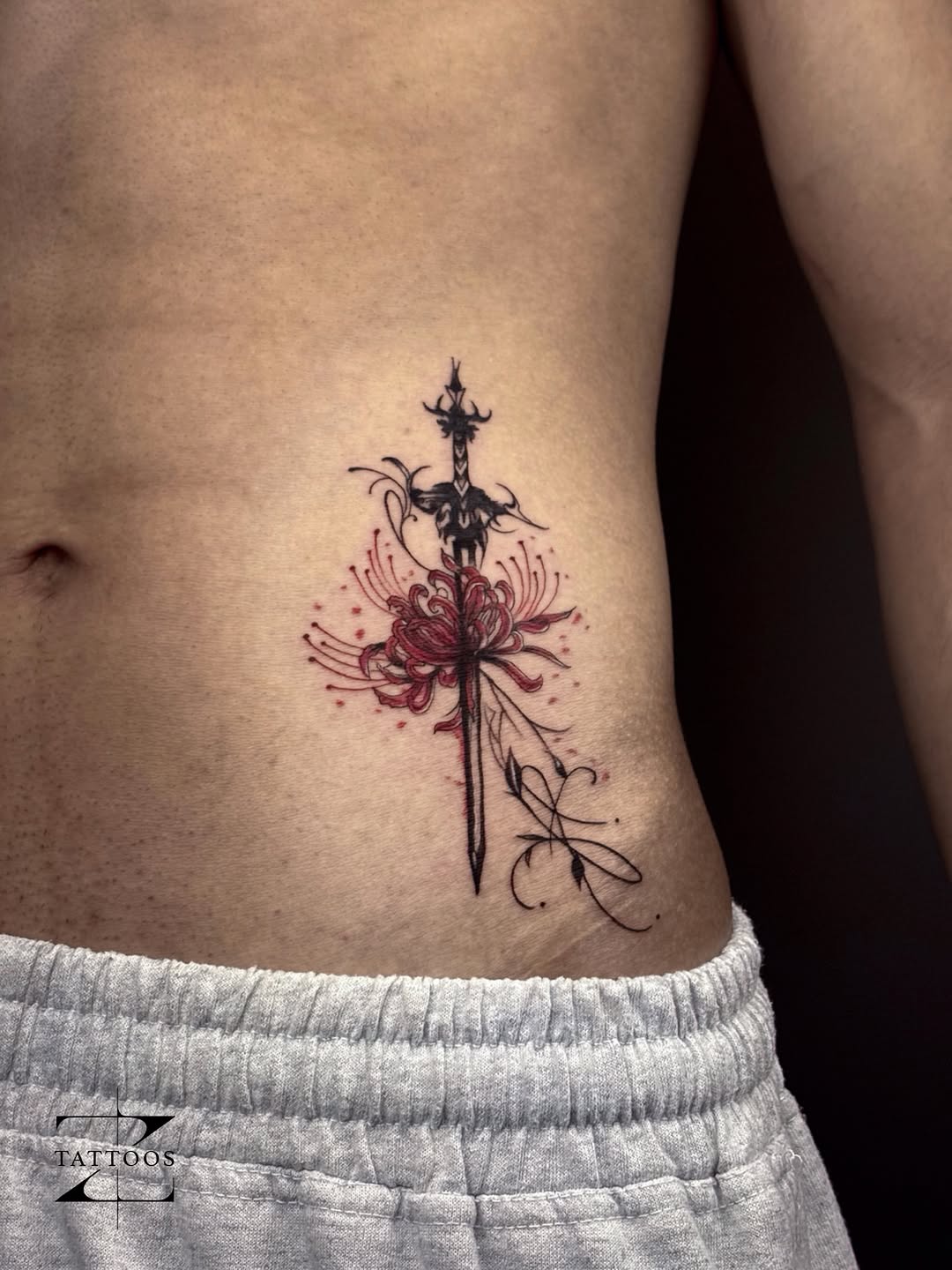Blackwork sword pierced through a red spider lily on the ribs.